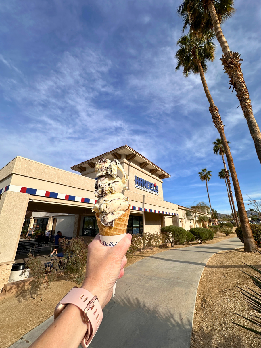 A triple scoop of ice cream held out in front of the exterior of Handel's Ice Cream in Palm Desert.