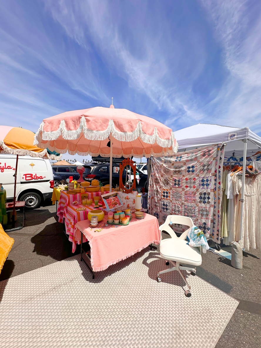 Shot of a vendor stall at the Palm Springs Vintage Market showing a pink umbrella covering a display of pink goods.