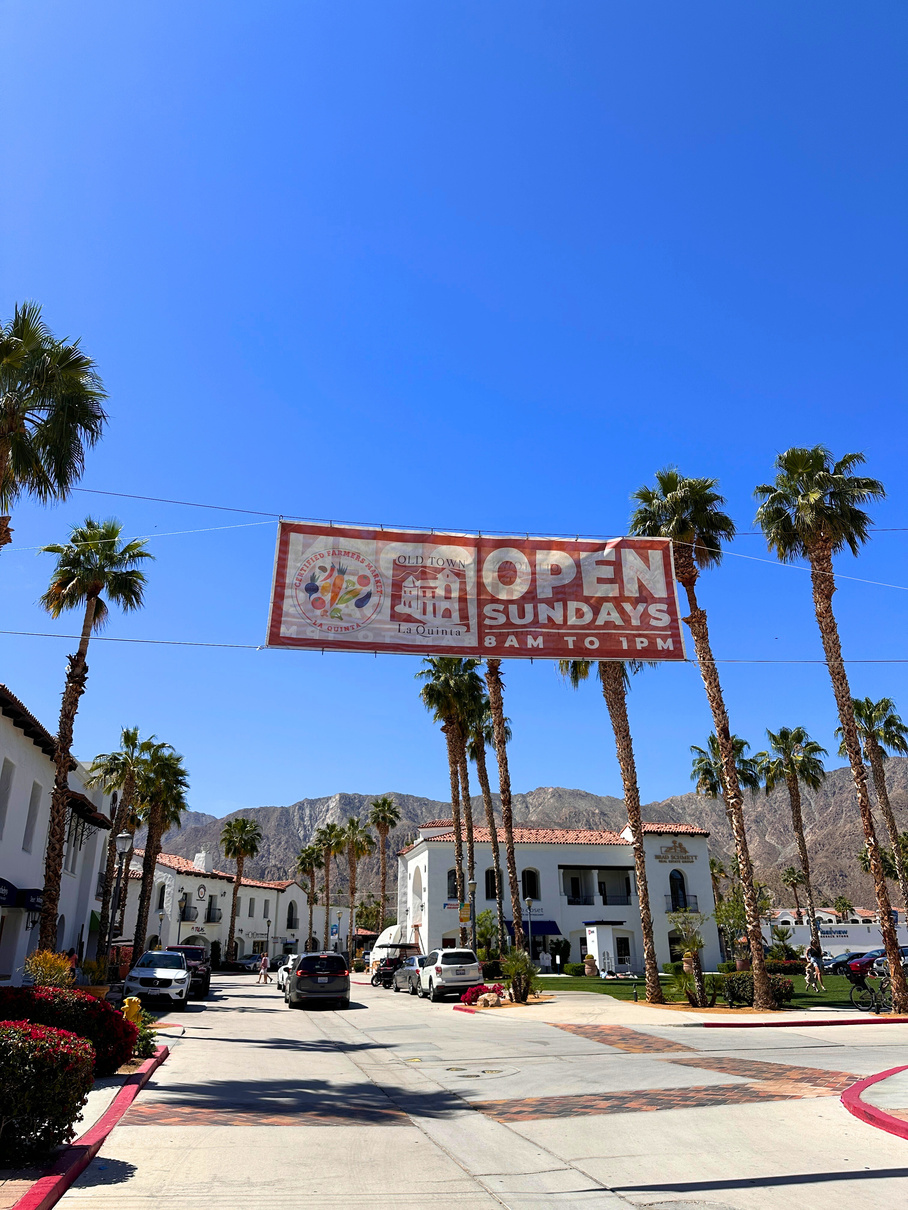 View of Old Town La Quinta with signage for the Old Town Farmers Market hanging in the foreground.